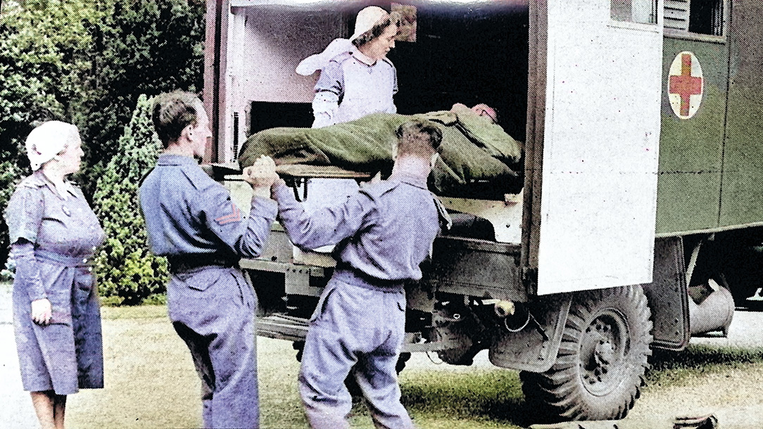 Four volunteers in blue clothing load a Red Cross ambulance