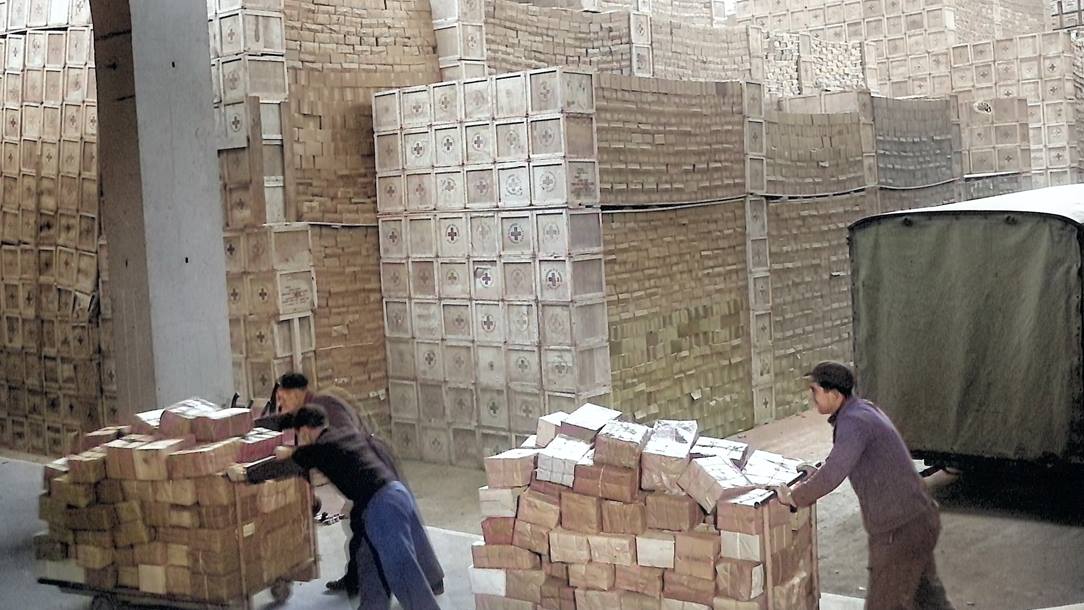 A warehouse packed with crates of Red Cross supplies and three volunteers pushing trolleys