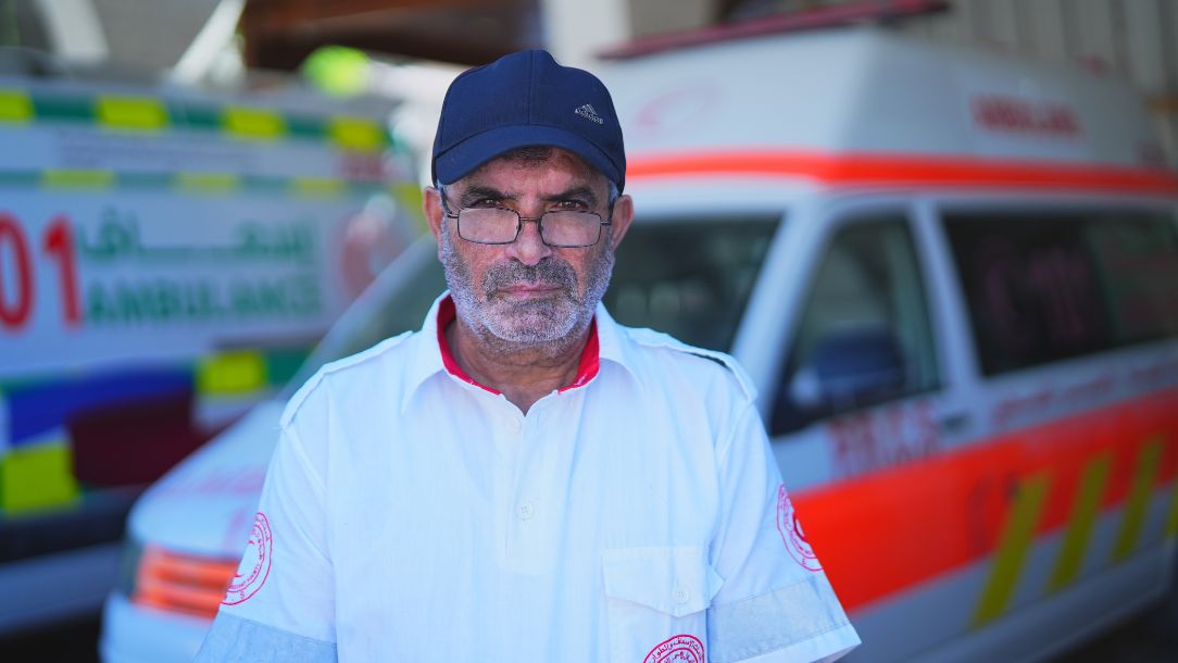 Awni from the Palestine Red Crescent Society stands in front of an ambulance, dressed in his uniform.