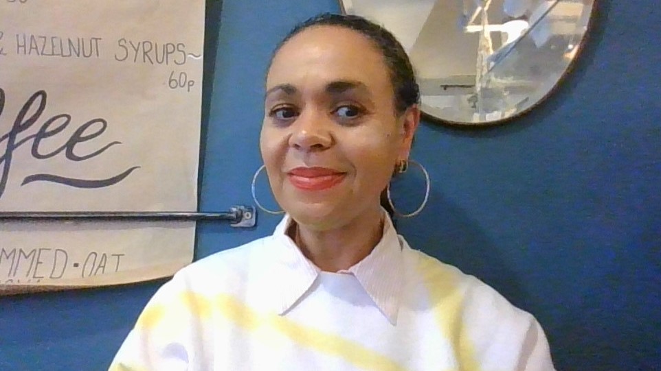 Fran smiles at camera. She has big hoop earrings, a white and yellow shirt and red lipstick