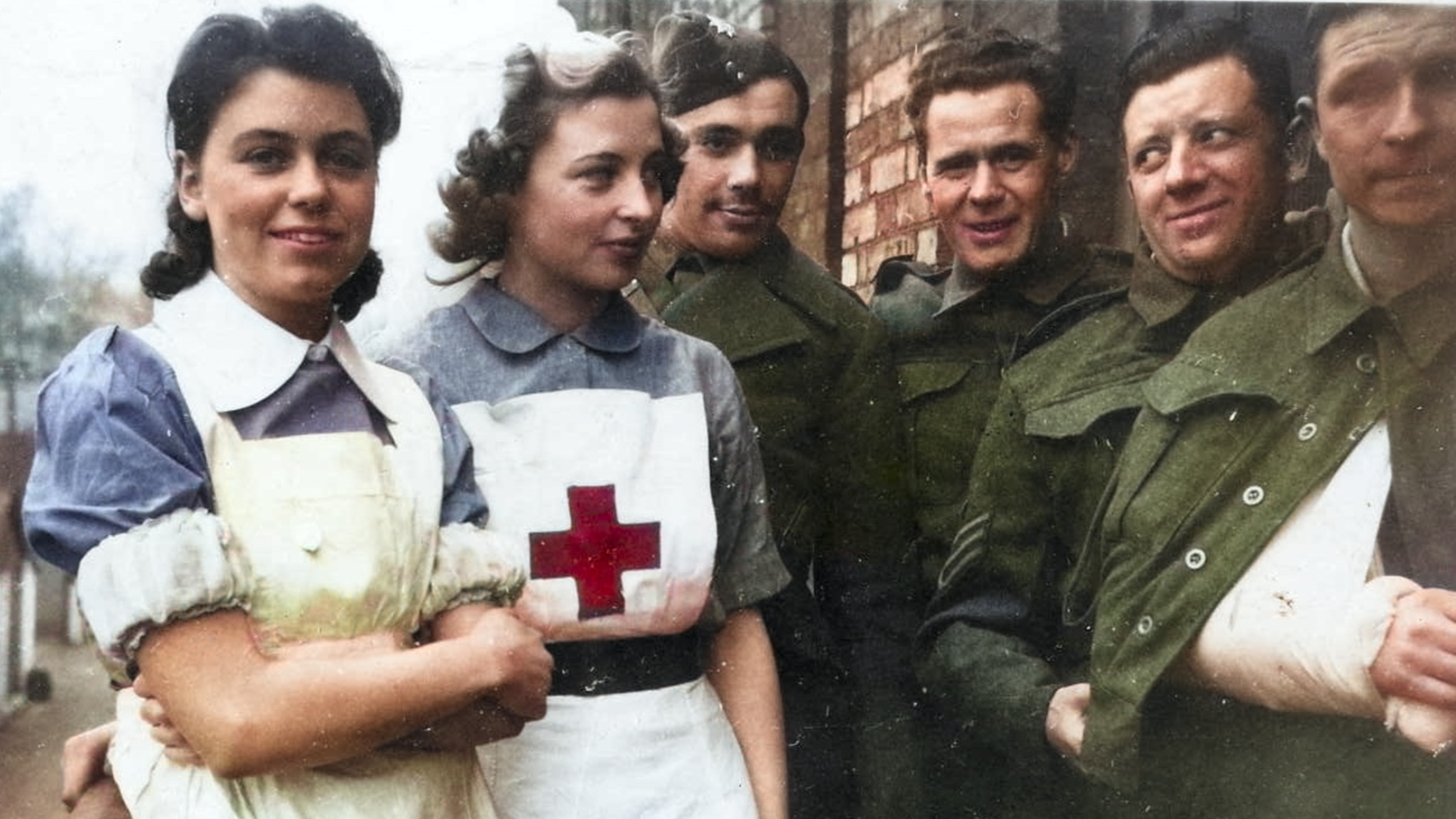 Two nurses and four soldiers in front of a brick building
