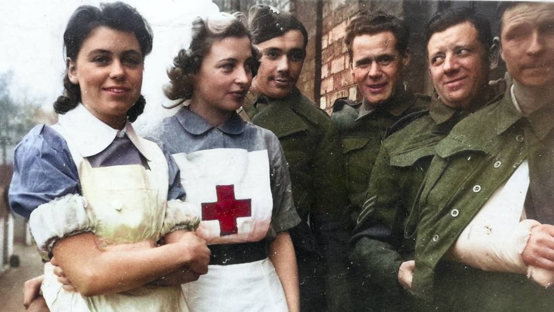 Two nurses and four soldiers in front of a brick building