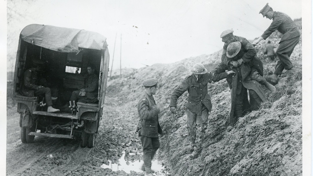 A photo of a group of soldiers during World War 1 helping eachother though mud towards an ambulance